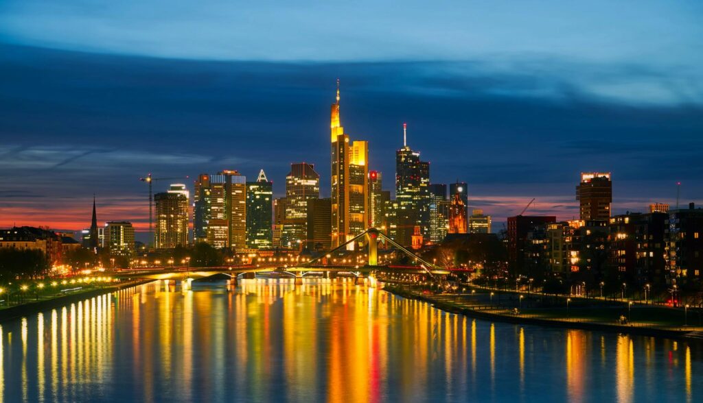 Frankfurt's illuminated skyline reflected in the river at night, showcasing iconic architecture and vibrant city lights.